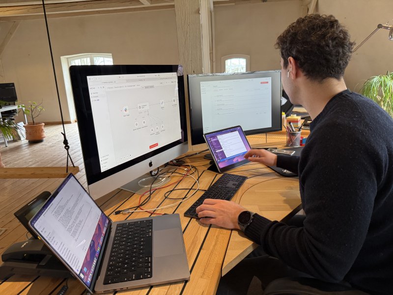 Ein junger Mann mit Kopfhörer arbeitet an Schreibtisch mit mehreren Bildschirmen, zeigt grafischen Workflow-Editor.